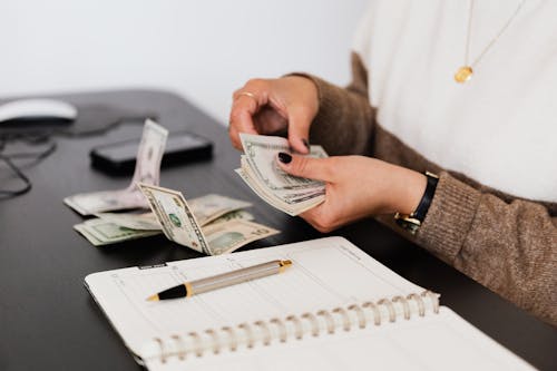 Free Close-up of person counting cash with notepad on desk, indicating financial tasks. Stock Photo