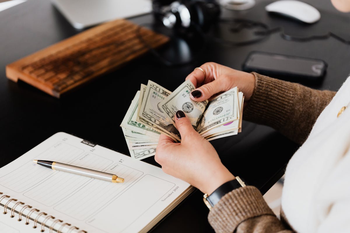 Woman reviewing expenses with a laptop and notebook at a kitchen table