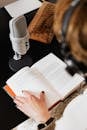 High angle of elegant female audiobook narrator recording audiobook while sitting at desk with microphone