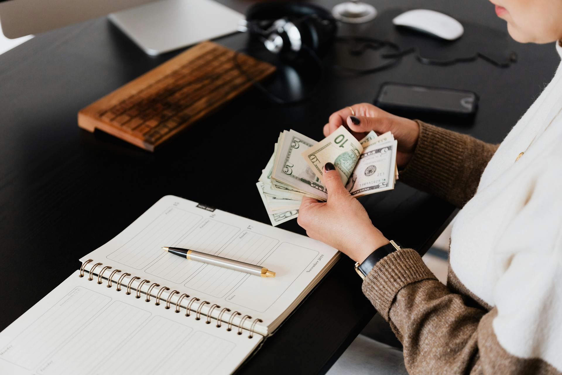 Person counting money at a desk with a planner, showcasing financial management and budgeting in a modern office setting.