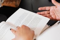 From above of crop anonymous female with manicured nails and thin gold rings reading book at desk