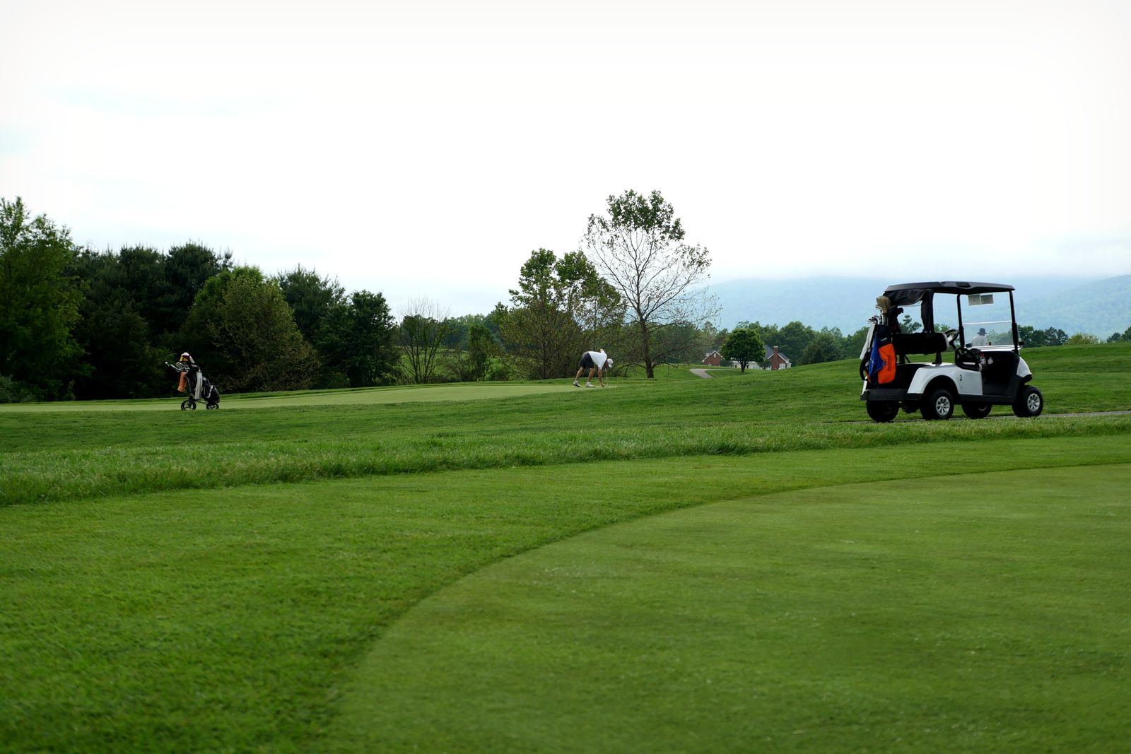 Golfers walking a lush green course under a cloudy sky