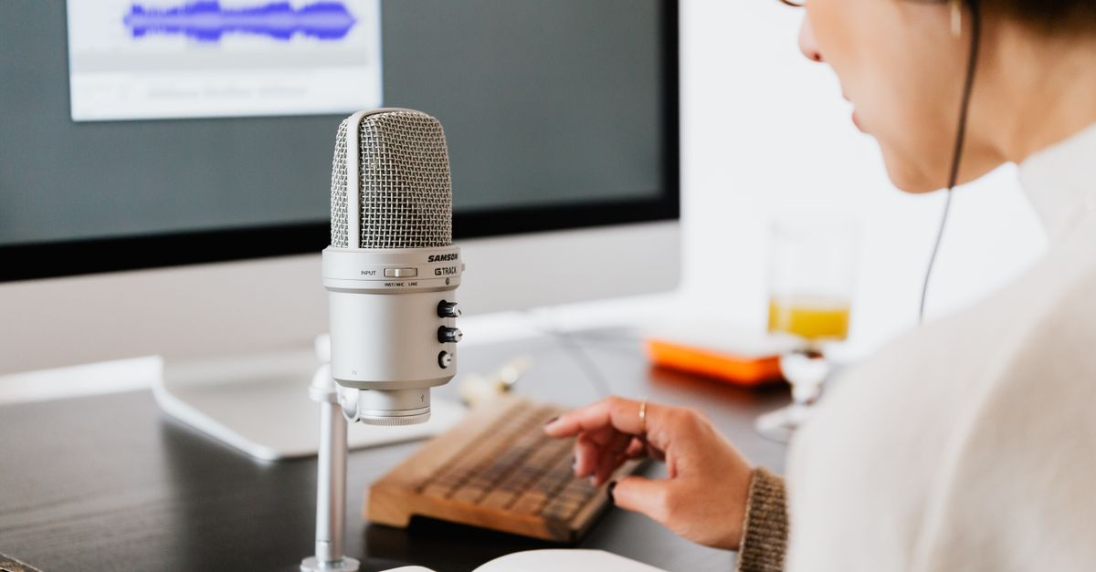 Persona usando auriculares y hablando por un micrófono en un estudio de grabación, con un libro abierto, representando la producción de contenido de audio.