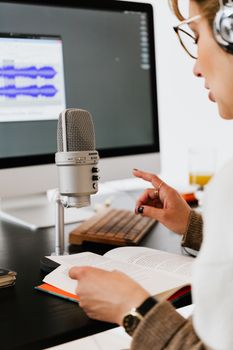 A person recording an audiobook using a professional microphone and headphones indoors.