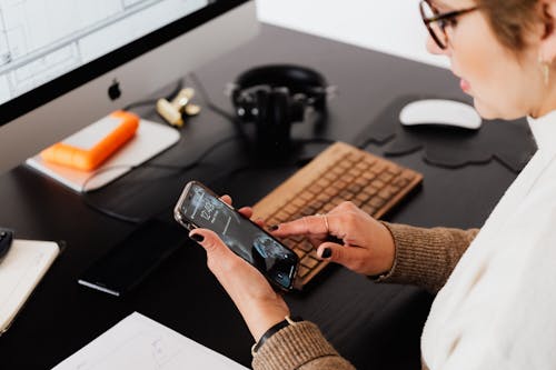 Free Crop woman using smartphone while working at computer Stock Photo
