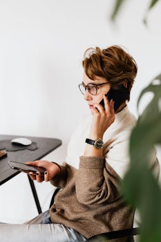 A young woman multitasks using two smartphones in a modern workspace setting.
