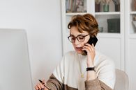 在现代办公室里，一位戴眼镜的短发女企业家正通过智能手机进行讨论