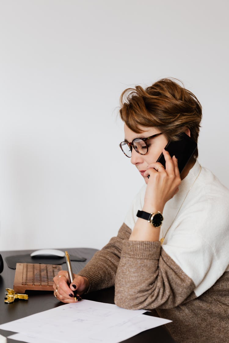 Smart Businesswoman Speaking On Smartphone And Writing On Paper In Office