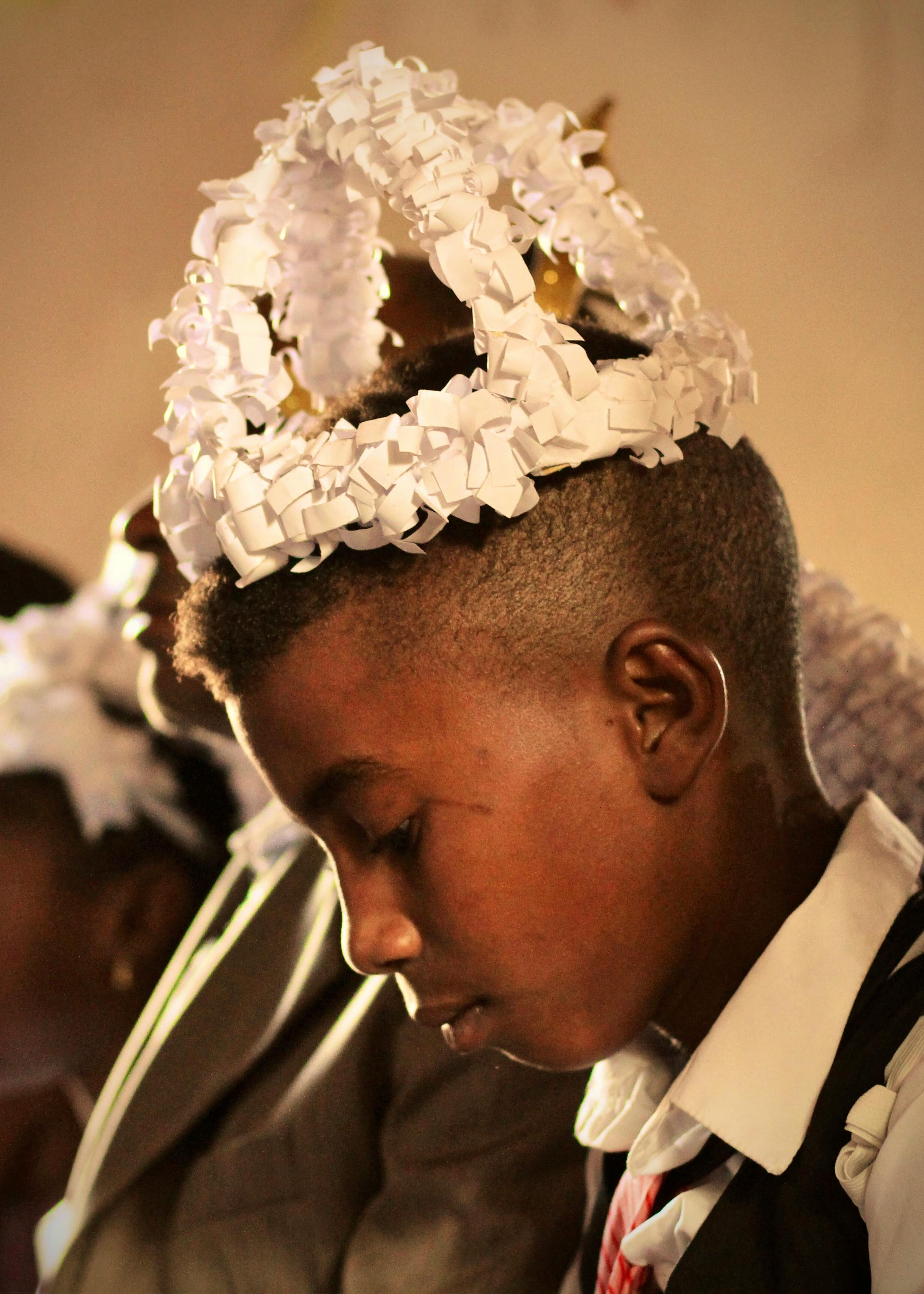 A boy with colorful headgear looks down in a thoughtful side profile portrait.