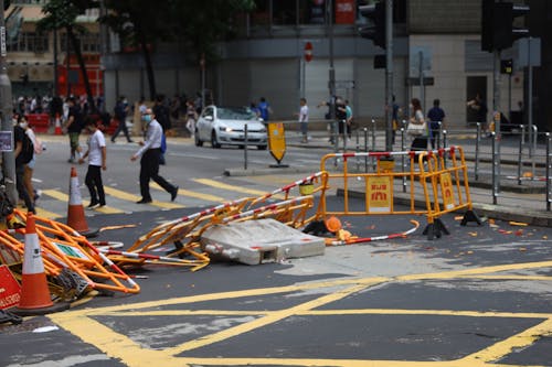 Crowd of people walking on sidewalk and pedestrian crossing on street with damaged fences after mass meetings