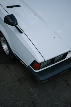 Close-up shot of a vintage white car's hood featuring a classic design with side mirror and headlight.