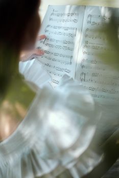 一位匿名女音乐家在高角度背影下阅读笔记本笔记，准备演奏乐器