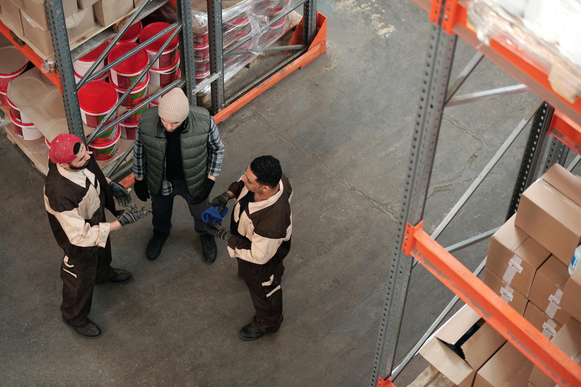 Three workers discussing logistics in an industrial warehouse setting from a high angle view.