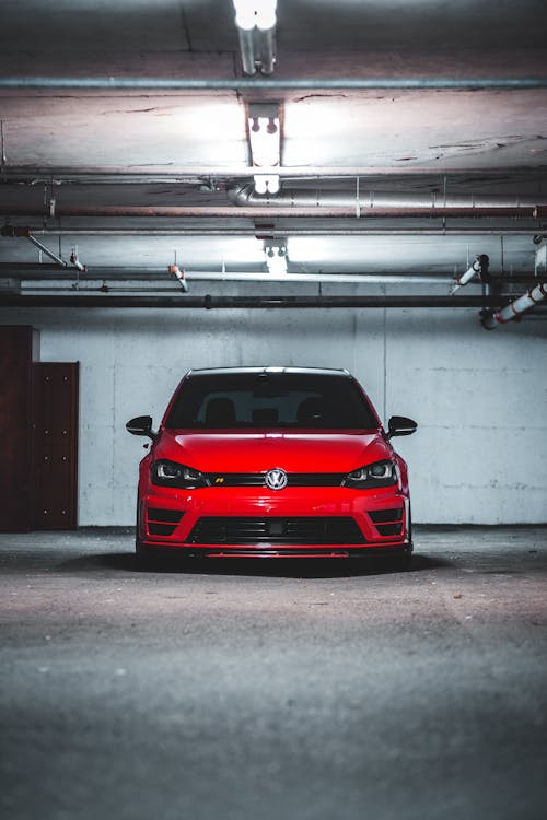 Contemporary shiny red car parked underground on asphalt parking lot under illuminated lamps