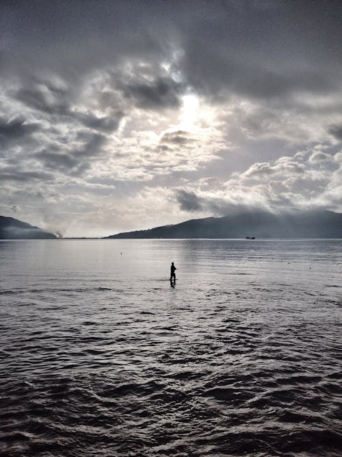 Silhouette Photo of a Person Standing on the Sea under Cloudy Sky
