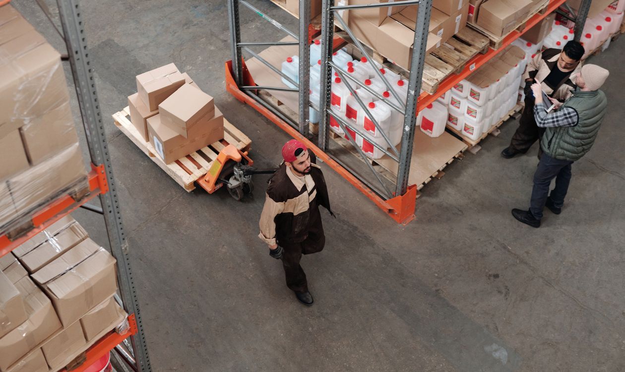 Warehouse staff checking order paperwork among stacked cartons on industrial shelving and pallets, illustrating order volume, minimum order quantities and supplier negotiation