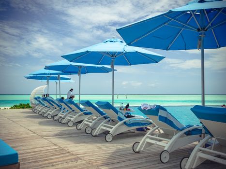 Collection of contemporary deck chairs under umbrellas located on wooden terrace in front of blue sea in summer