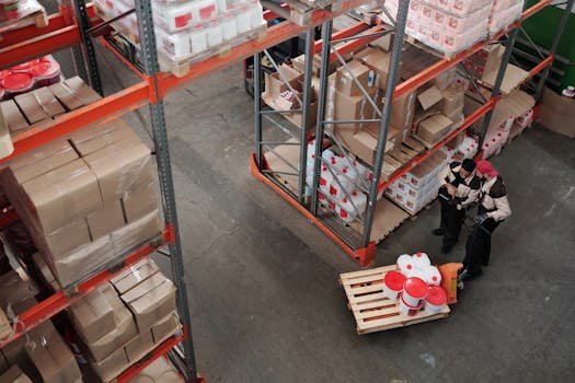 Workers managing inventory on shelves in a warehouse, viewed from above.