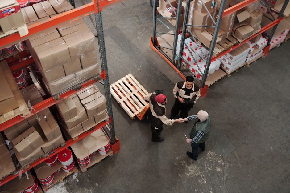 Warehouse workers shaking hands over pallets, seen from above.