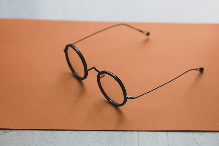 Close-Up Photo Of A Black Framed Round Eyeglasses On Orange Surface