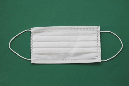 Free White surgical mask placed against a vibrant green background for health safety themes. Stock Photo