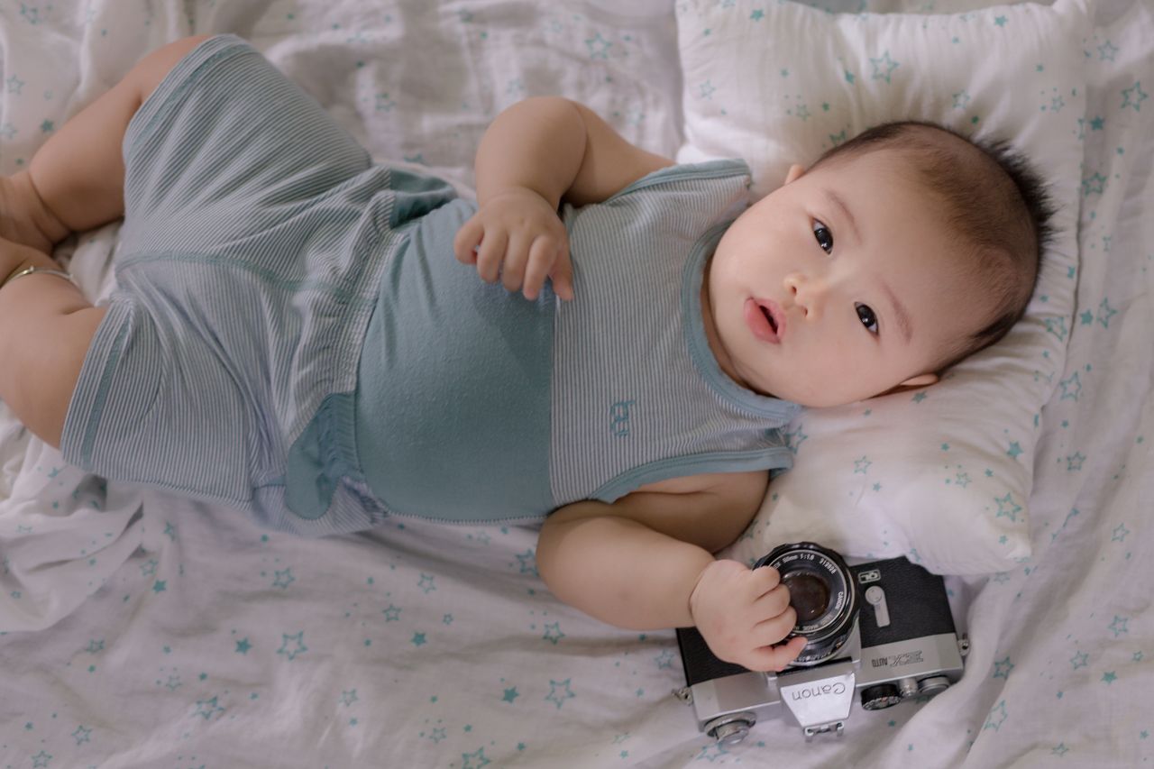 top view of cute infant asian child holding photo camera while lying o