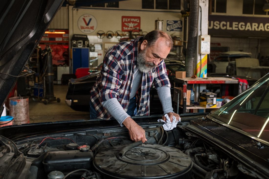 A mechanic in a plaid flannel shirt working over an engine in the shop