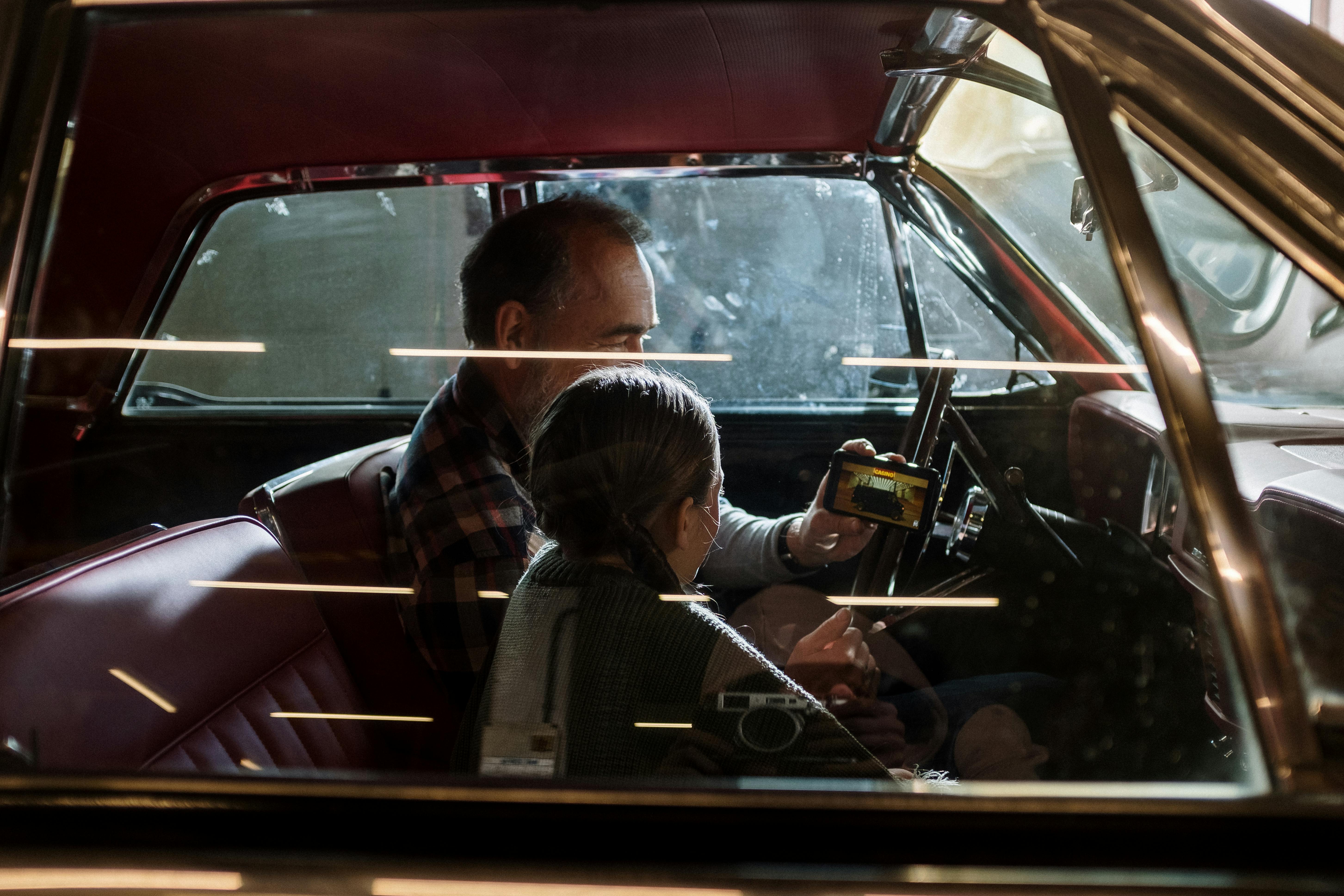 a man and his daughter looking at the phone while sitting in the car