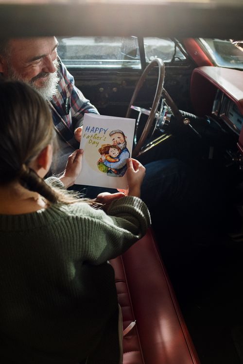Free A tender moment between a father and daughter sharing a greeting card in a vintage car. Stock Photo