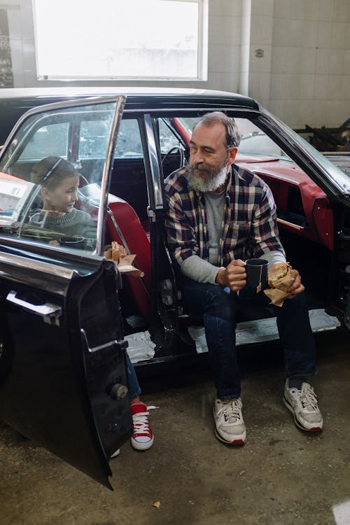 Man in Brown and White Plaid Dress Shirt and Blue Denim Jeans Sitting on Red Car