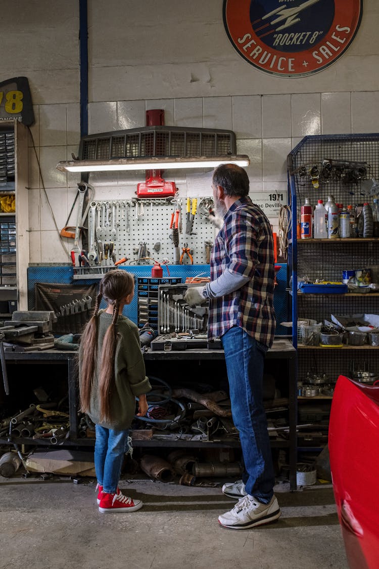 Back View Of A Mechanic And His Daughter Looking At Tools In The Garage