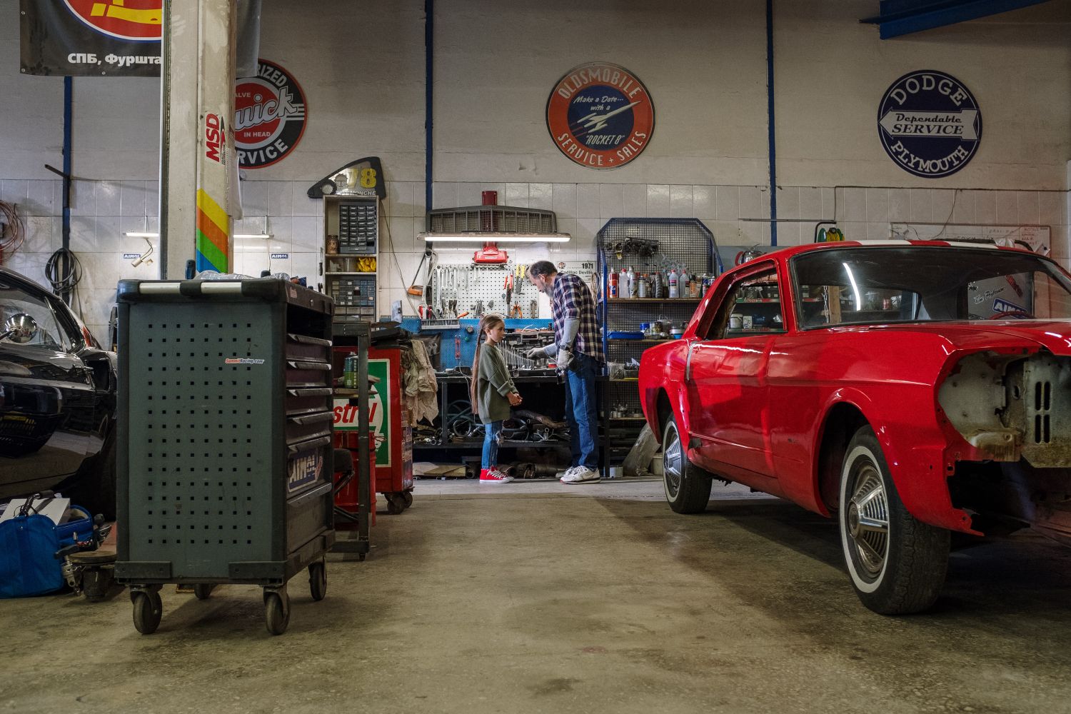 Father and daughter working on a classic red Mustang together in a vintage tool-filled garage on Father's Day