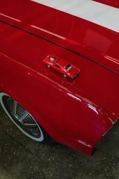 在红色背景下，一辆微型红色玩具车放置于老式汽车之上，展示着经典设计