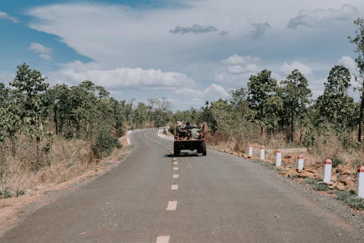 A vehicle travels a winding rural road through a lush forest, capturing the essence of adventure and nature.