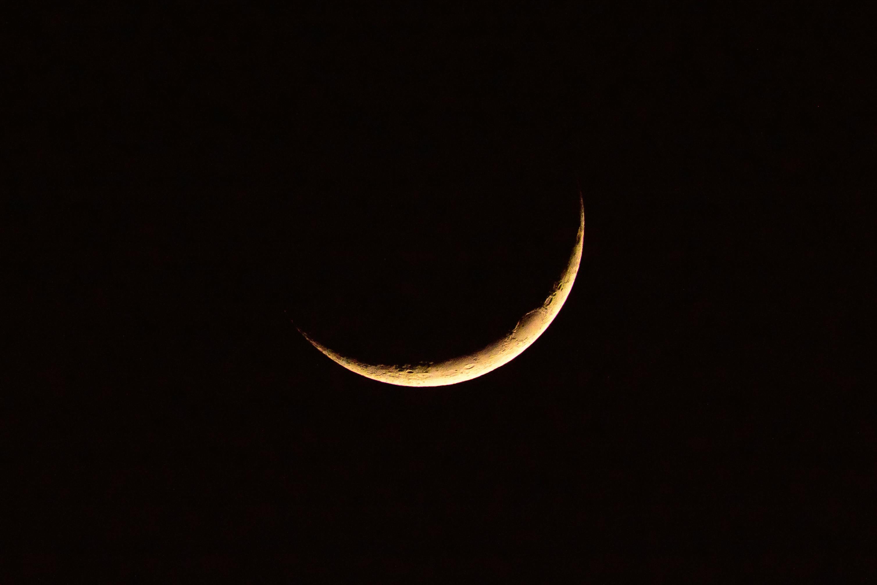 Astronomical natural background with bright yellow crescent moon glowing on dark black sky
