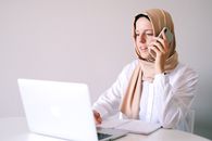 一位戴着头巾的女商人在家庭办公室里用笔记本电脑和手机处理多项任务