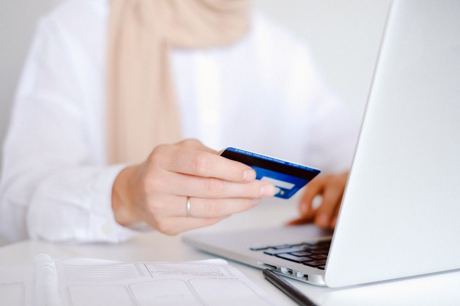 Close-up of a person holding a credit card while using a laptop for online shopping.