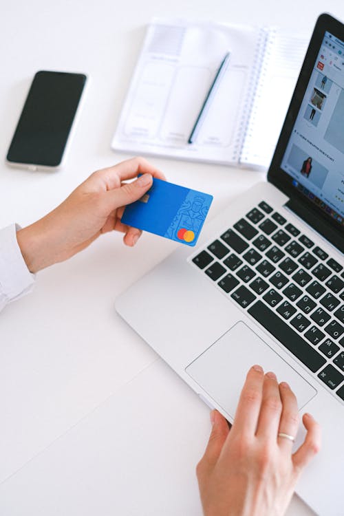 Person Using a Laptop and Looking at a Debit Card