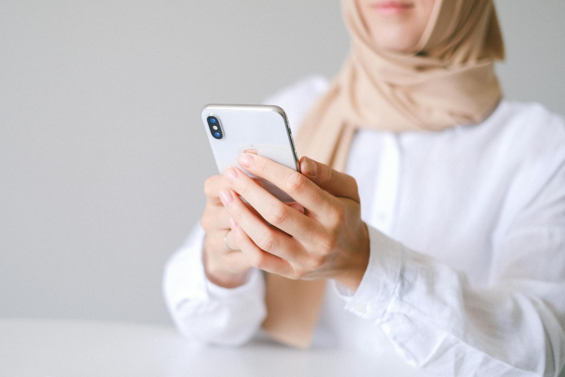 Woman in hijab using smartphone in a minimalist indoor setting, focused on technology and communication.