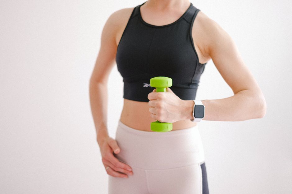 Withings ScanWatch 2 vs Apple Watch: Health Monitoring Showdown (2024) A woman in activewear using a dumbbell and smartwatch during a home workout.