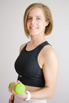 Portrait of a woman in activewear holding a dumbbell, smiling confidently.