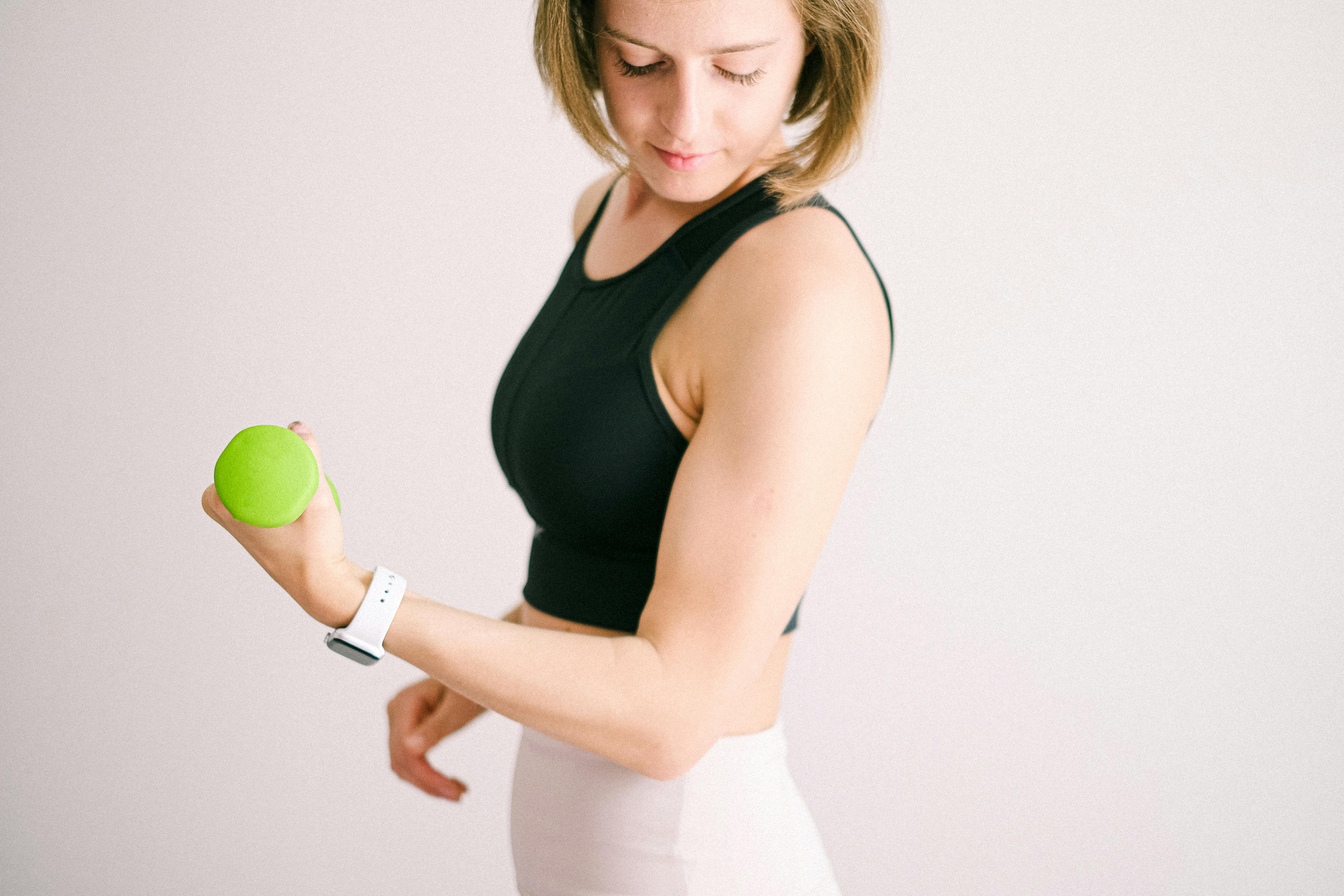 Adult woman in activewear exercising with a green dumbbell indoors.