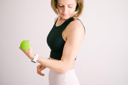 Adult woman in activewear exercising with a green dumbbell indoors.