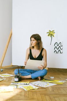 一名妇女若有所思地坐在工作室的地板上，周围都是她的艺术作品