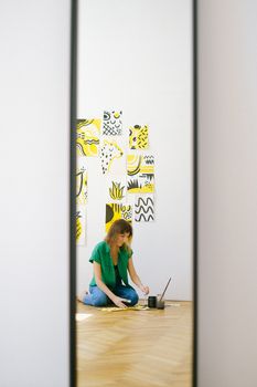 一名妇女在工作室的地板上画画，镜子里映出她的倒影