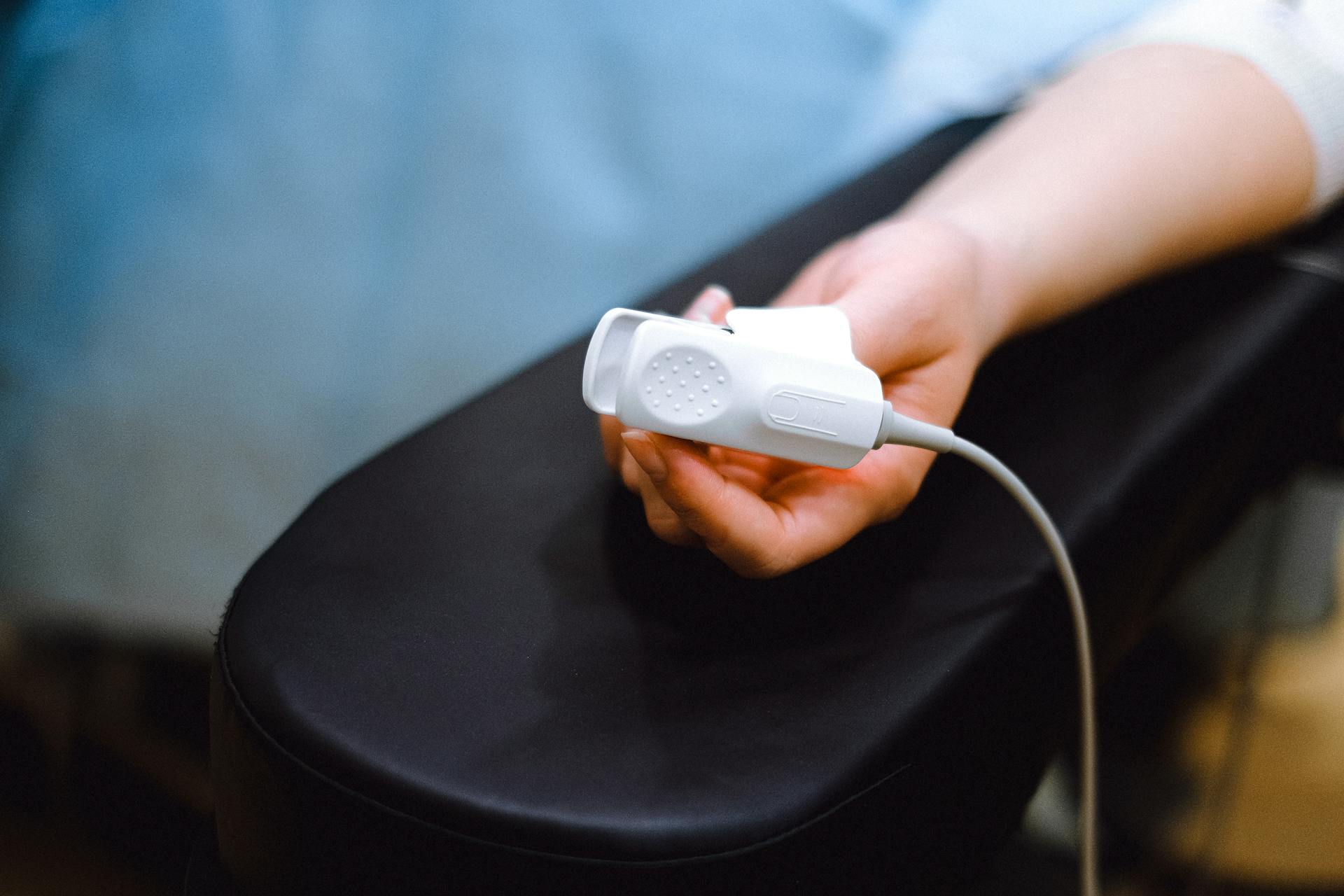 A hand holds a medical device on an armrest, suggesting healthcare context.