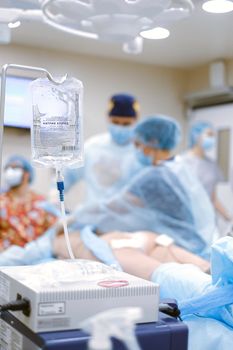 Medical team performs surgery with focus on IV drip in a hospital operating room.