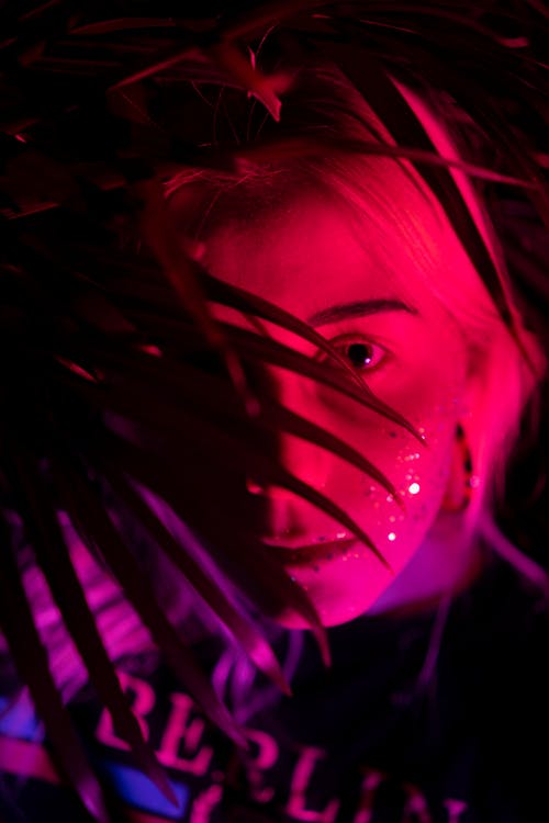 Woman with shiny sparkles on face in neon illumination