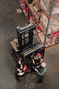 Warehouse employees discussing logistics around a forklift in an industrial setting.