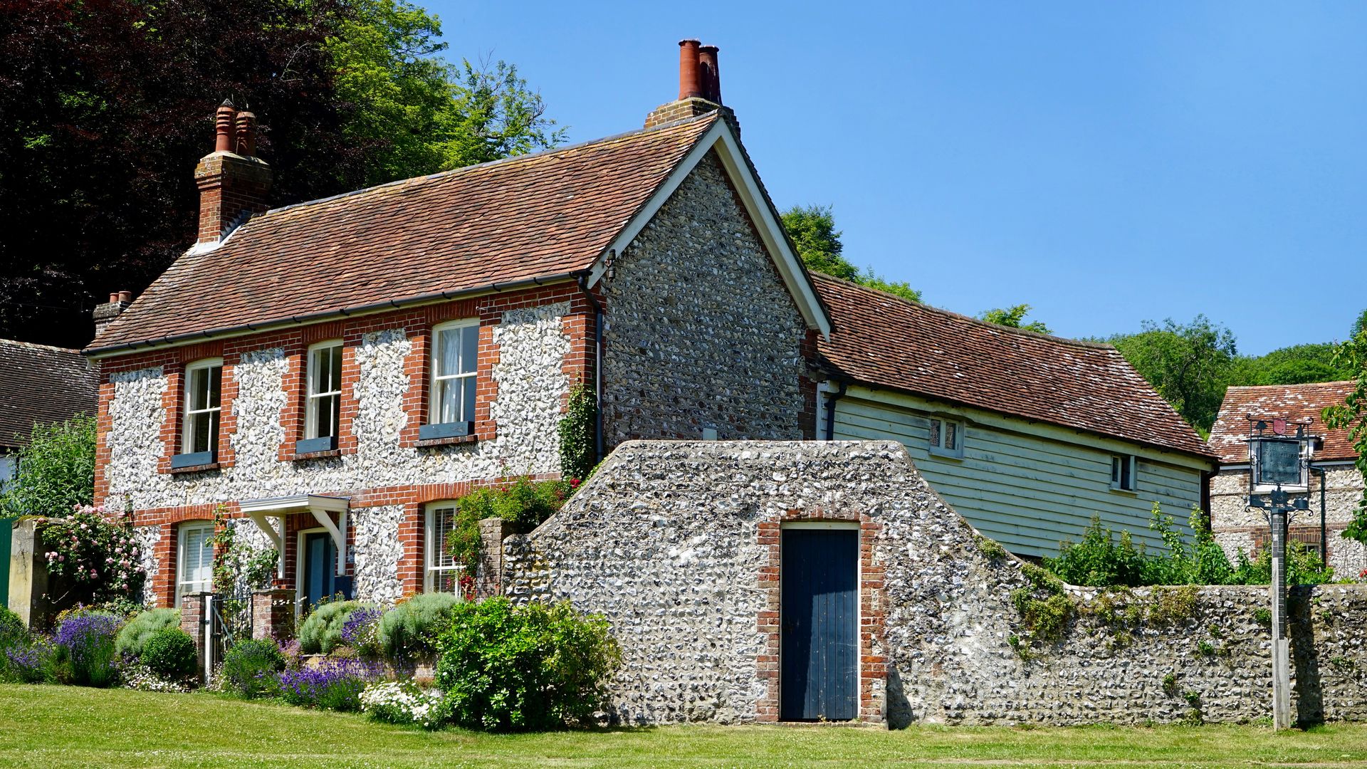 Beautiful countryside home with stone facade and lush garden under a blue sky.